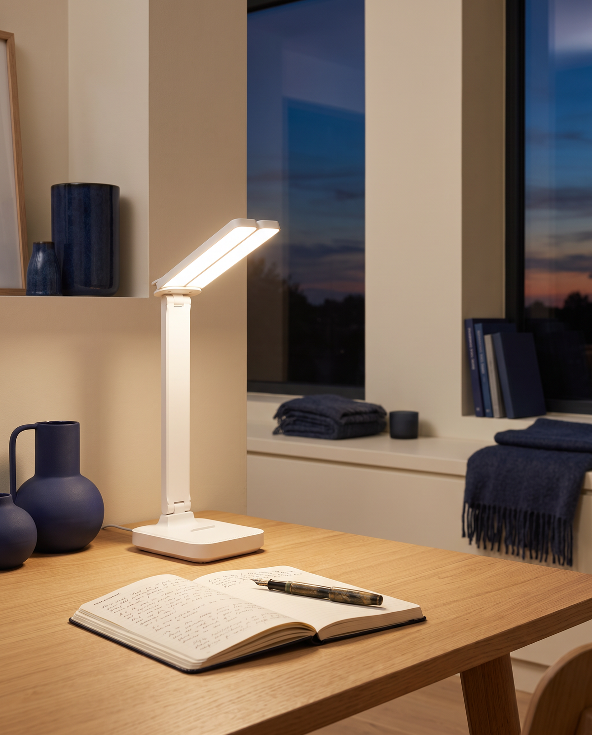 Lampe de bureau allumée le soir éclairant un carnet sur un bureau en chêne