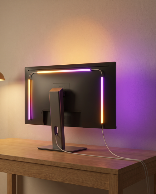 Bande LED RGBIC fixée au dos d'un écran, halo coloré sur le mur