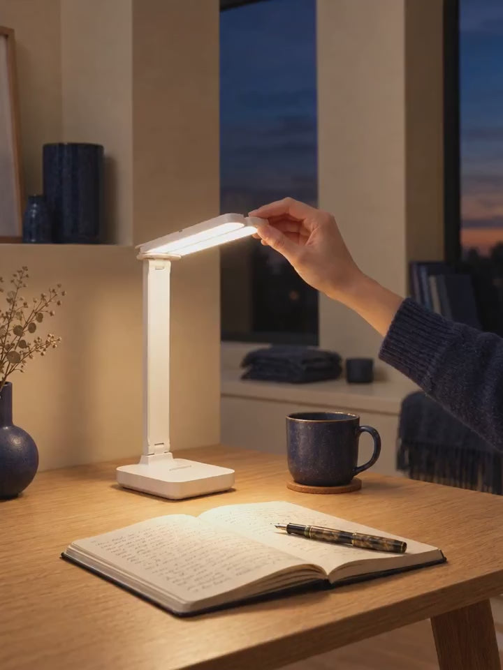 Main qui oriente la lampe de bureau pliable VALORIA sur un carnet le soir